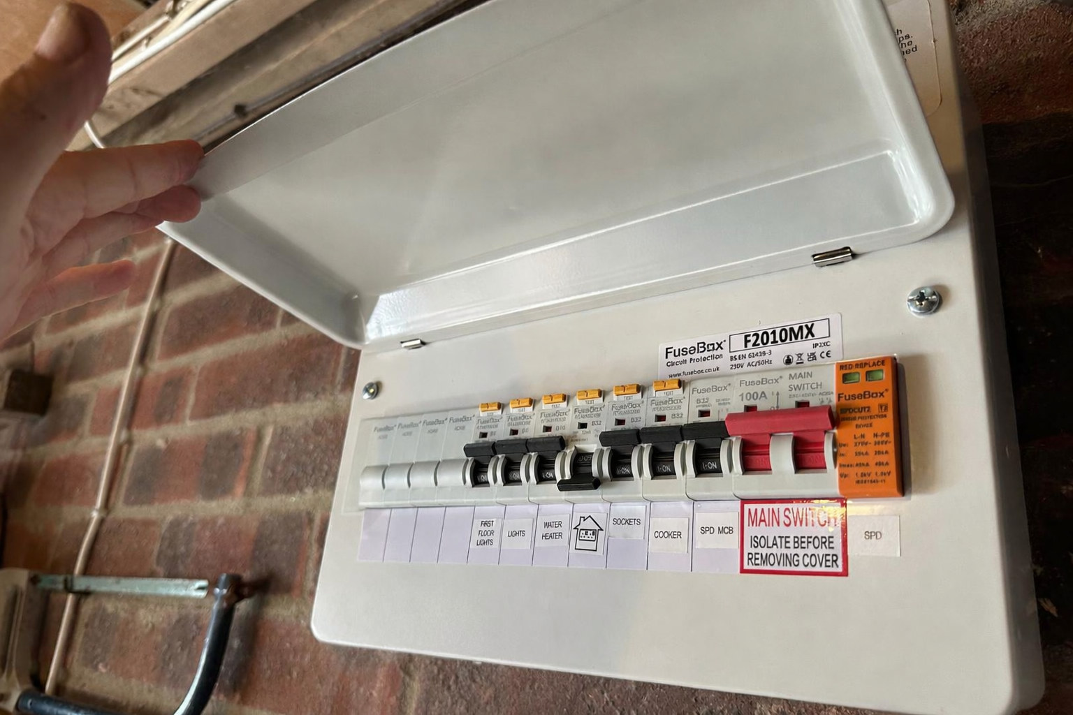 Electrician lifting the cover off a consumer unit to inspect the circuit breakers