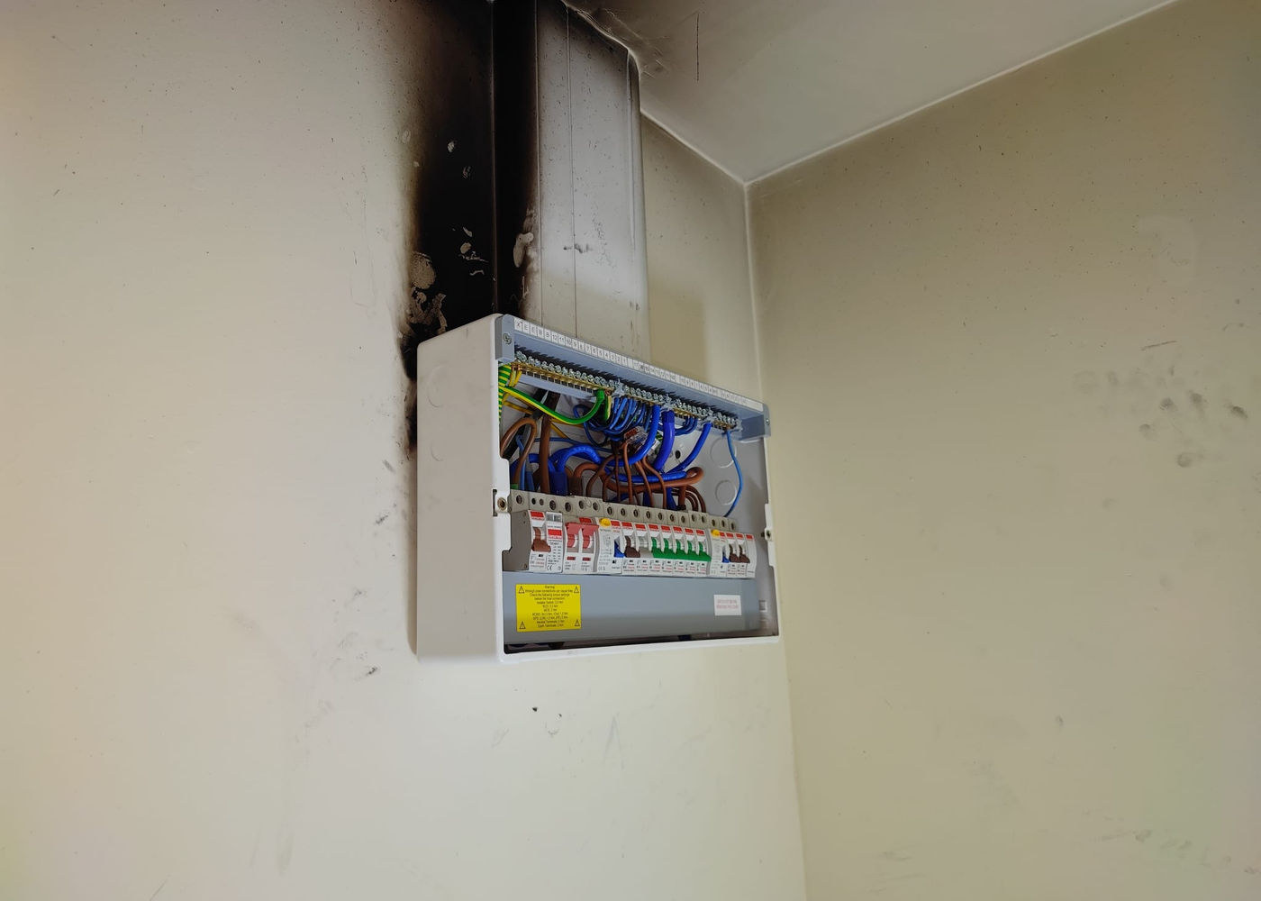 Consumer unit with its cover removed, below heavy scorch damage to the trunking above it