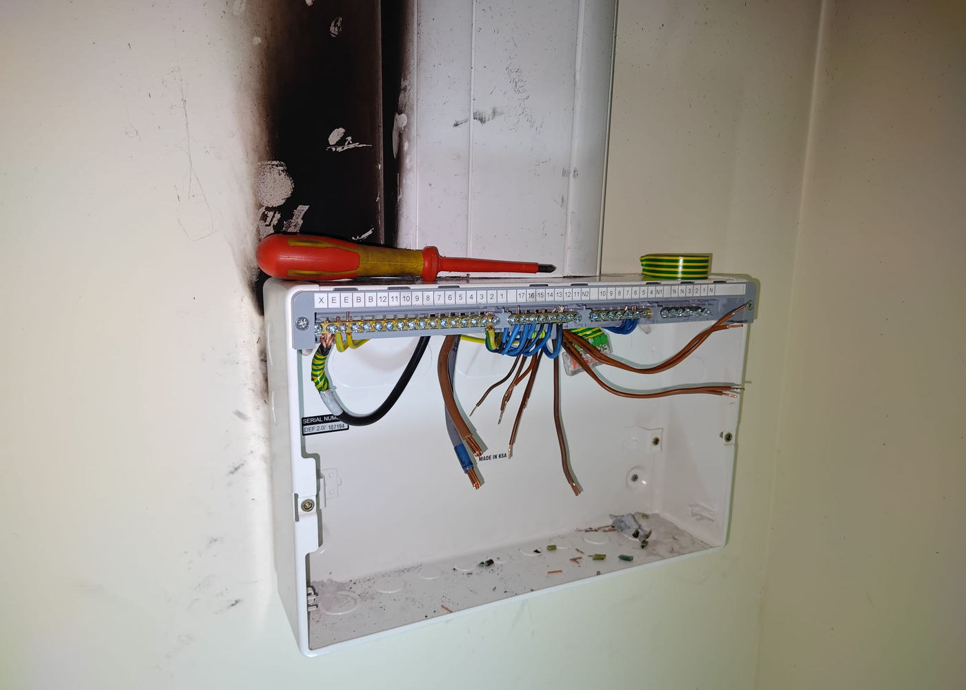Fire-damaged consumer unit back box with a screwdriver and insulation tape left on top during repair