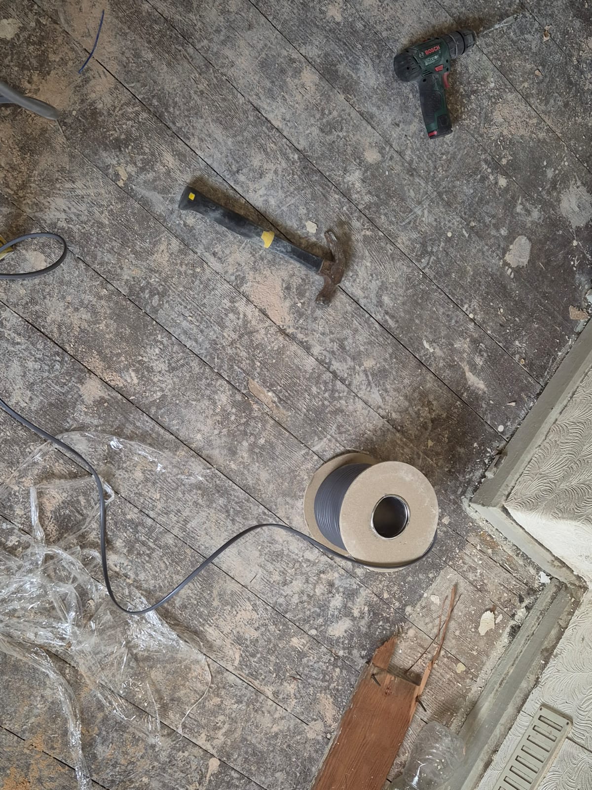 Hammer, drill and cable reel laid out on a stripped floor during a rewire
